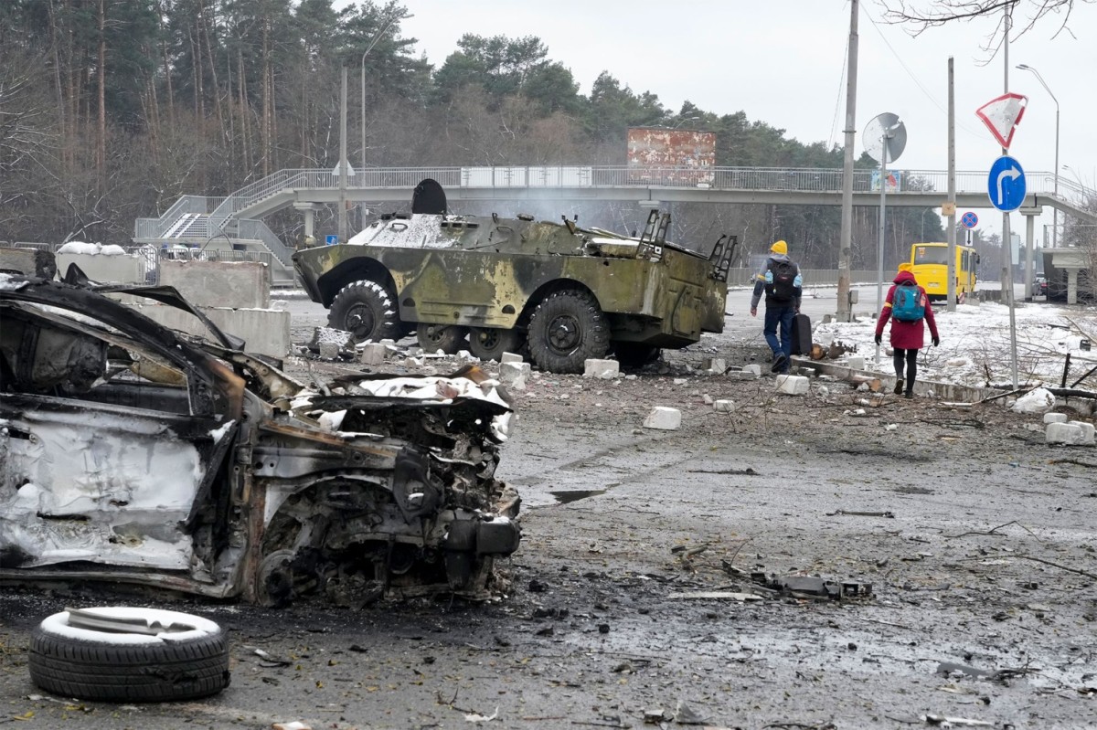 People walk by a damaged vehicle and an armored car at a checkpoint in Brovary, outside Kyiv.